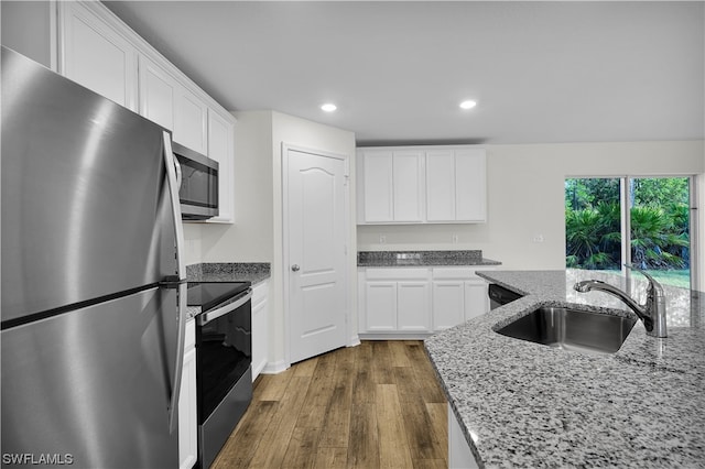 kitchen with sink, light stone counters, hardwood / wood-style floors, appliances with stainless steel finishes, and white cabinetry