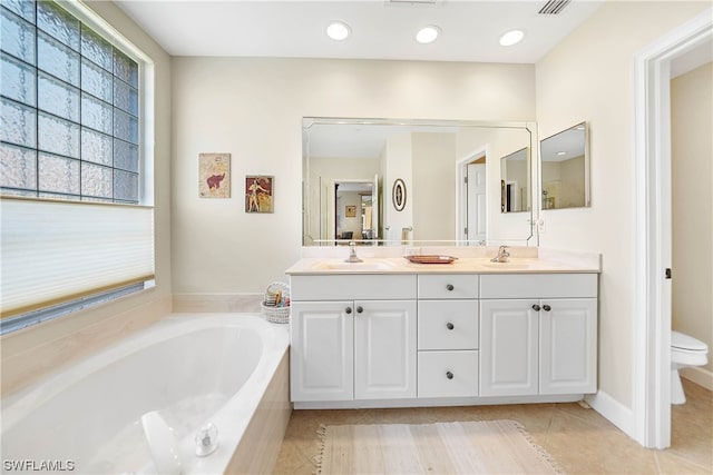 bathroom featuring a relaxing tiled bath, toilet, dual bowl vanity, and tile flooring