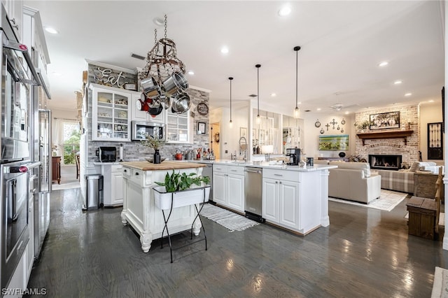 kitchen featuring white cabinets, stainless steel appliances, dark hardwood / wood-style flooring, and a brick fireplace