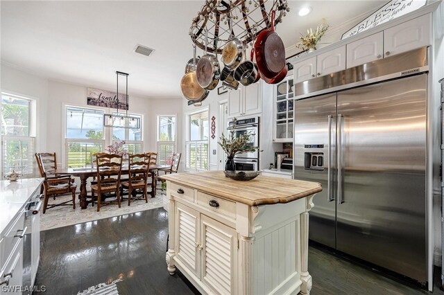 kitchen with butcher block countertops, a center island, dark wood-type flooring, appliances with stainless steel finishes, and white cabinetry