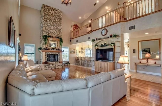 living room featuring a chandelier, light hardwood / wood-style floors, a stone fireplace, and high vaulted ceiling