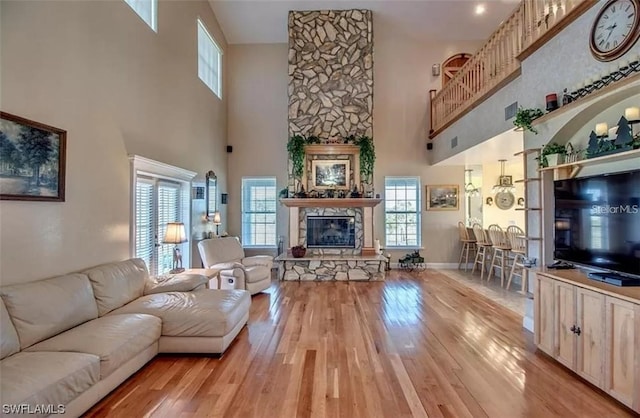 living room featuring a healthy amount of sunlight, light hardwood / wood-style floors, a towering ceiling, and a fireplace