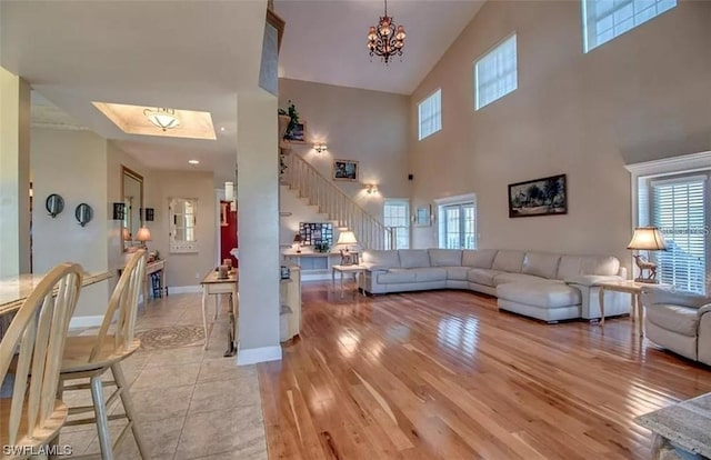 living room with an inviting chandelier, a skylight, high vaulted ceiling, and light tile floors