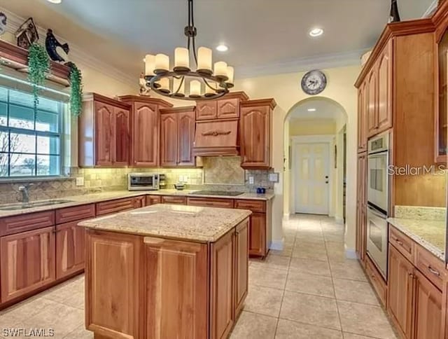 kitchen with a chandelier, light tile floors, a center island, tasteful backsplash, and crown molding