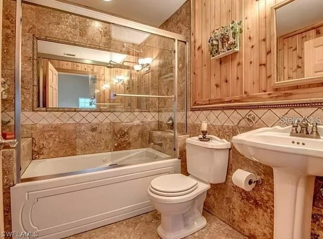 bathroom featuring tile floors, toilet, bath / shower combo with glass door, and tasteful backsplash