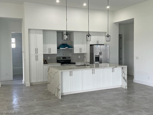 kitchen with a kitchen island with sink, appliances with stainless steel finishes, sink, wall chimney exhaust hood, and pendant lighting