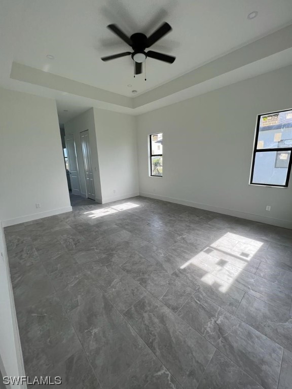 unfurnished room with dark tile flooring, a tray ceiling, and ceiling fan