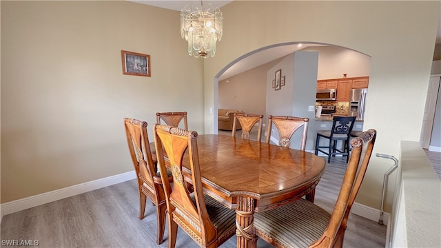 dining room featuring light wood-type flooring, a towering ceiling, and an inviting chandelier