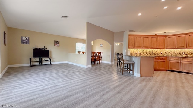 kitchen with a breakfast bar, light wood-type flooring, light stone countertops, and tasteful backsplash