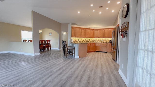 kitchen featuring light stone counters, stainless steel refrigerator, a kitchen breakfast bar, decorative backsplash, and light hardwood / wood-style flooring