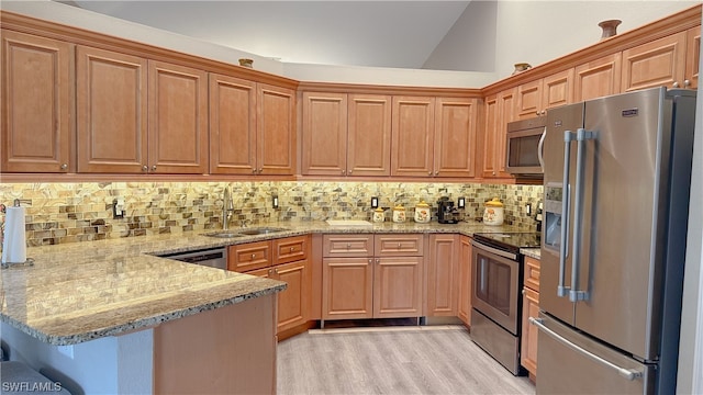 kitchen featuring appliances with stainless steel finishes, kitchen peninsula, light stone countertops, lofted ceiling, and sink