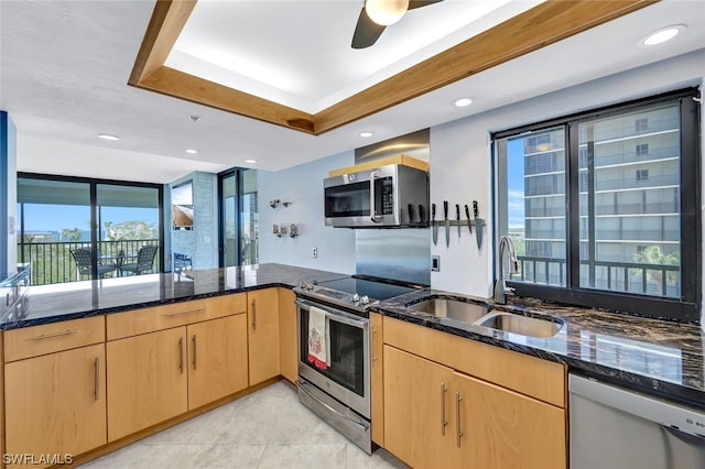 kitchen with light brown cabinets, sink, dark stone countertops, kitchen peninsula, and stainless steel appliances