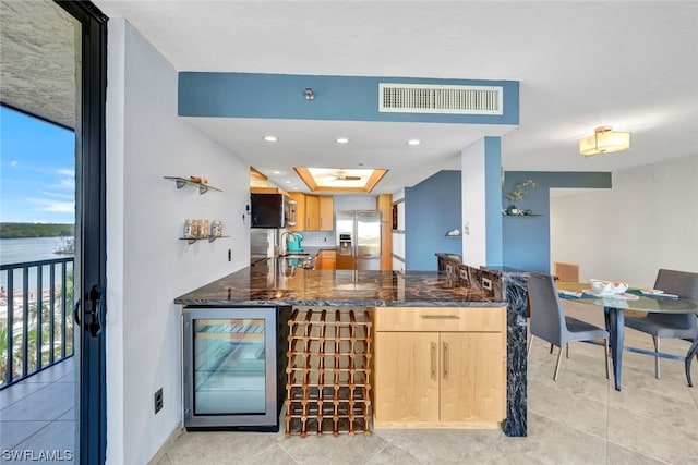 kitchen with wine cooler, stainless steel fridge with ice dispenser, kitchen peninsula, dark stone countertops, and light brown cabinetry