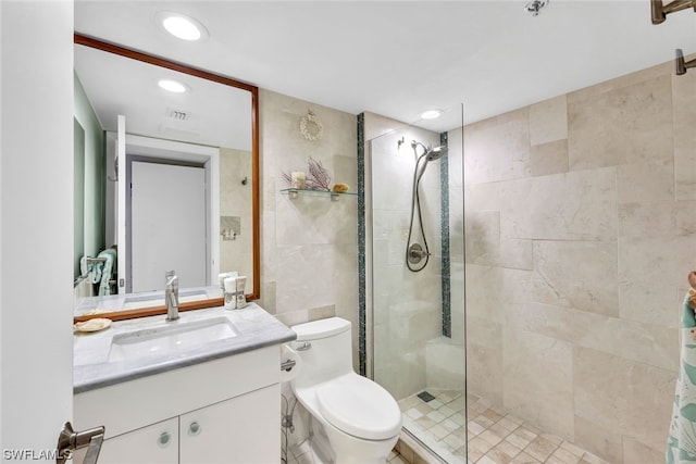 bathroom with vanity, toilet, tiled shower, and tile walls