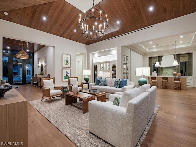 living room with a notable chandelier, wood ceiling, light hardwood / wood-style flooring, a towering ceiling, and a raised ceiling