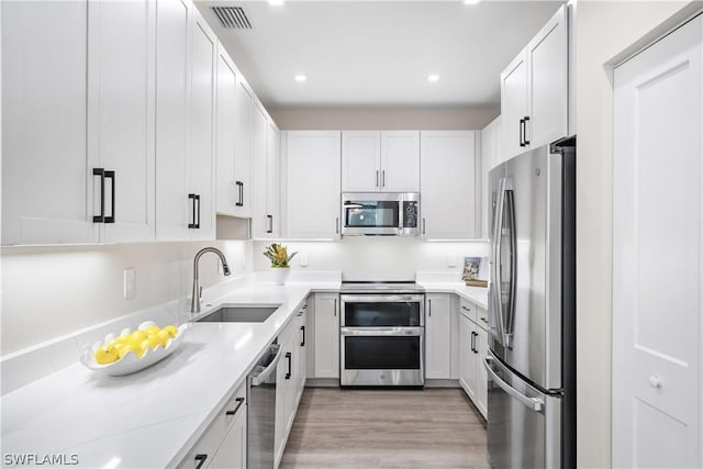 kitchen with light stone countertops, appliances with stainless steel finishes, sink, light hardwood / wood-style flooring, and white cabinetry