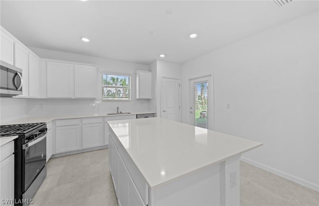 kitchen with a kitchen island, appliances with stainless steel finishes, white cabinetry, and light tile flooring