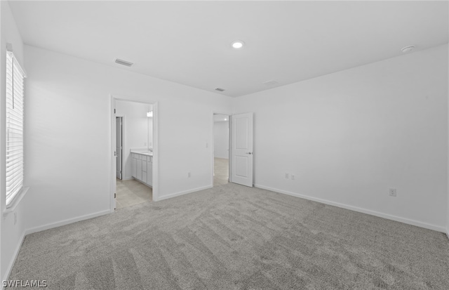 unfurnished bedroom featuring light carpet and ensuite bath