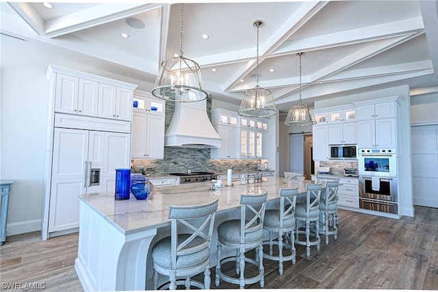 kitchen with decorative light fixtures, white cabinetry, black microwave, a large island, and custom range hood