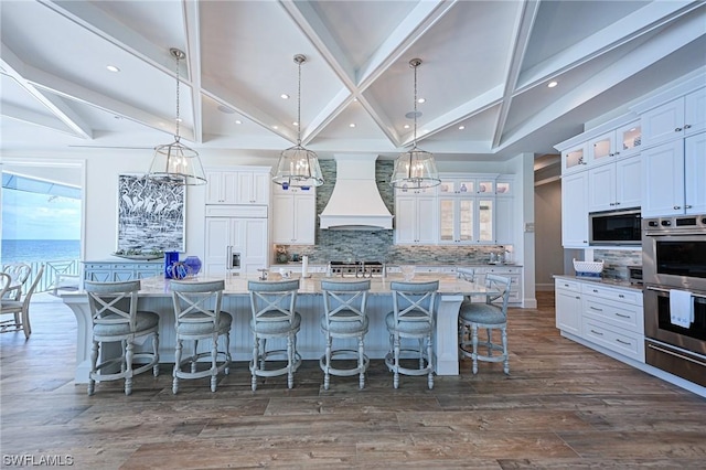 kitchen featuring premium range hood, a breakfast bar, hanging light fixtures, a large island with sink, and built in appliances