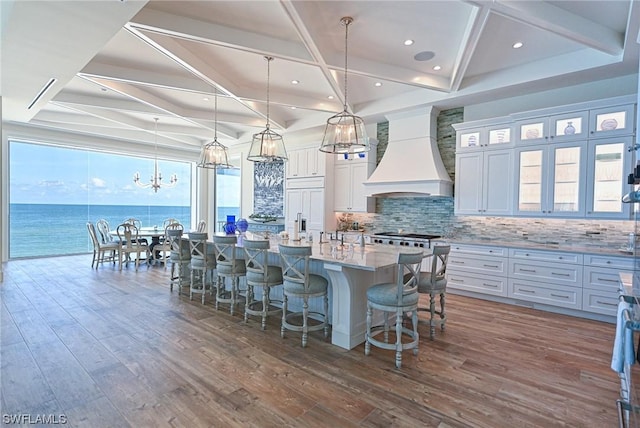 kitchen featuring premium range hood, pendant lighting, white cabinetry, a large island with sink, and a water view