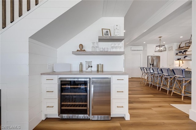 bar featuring white cabinets, stainless steel fridge, beverage cooler, and light hardwood / wood-style flooring