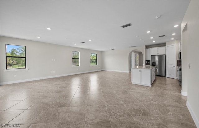 kitchen featuring stainless steel fridge, light tile flooring, a kitchen island with sink, and white cabinetry