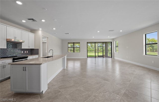 kitchen featuring light tile flooring, sink, a center island with sink, range with electric stovetop, and light stone counters