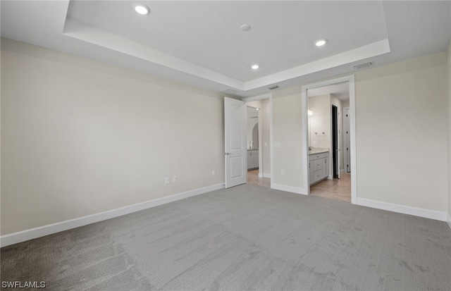 unfurnished bedroom featuring light carpet, ensuite bath, and a tray ceiling