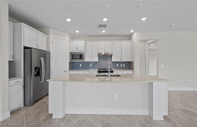 kitchen featuring white cabinets, light stone countertops, a center island with sink, and appliances with stainless steel finishes