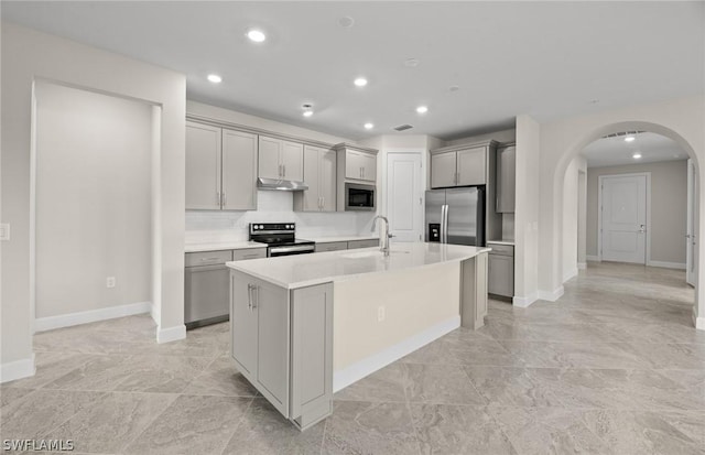 kitchen with decorative backsplash, gray cabinetry, stainless steel appliances, sink, and a center island with sink