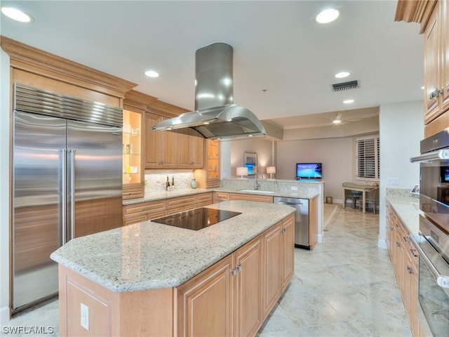 kitchen with sink, appliances with stainless steel finishes, light stone counters, island exhaust hood, and kitchen peninsula