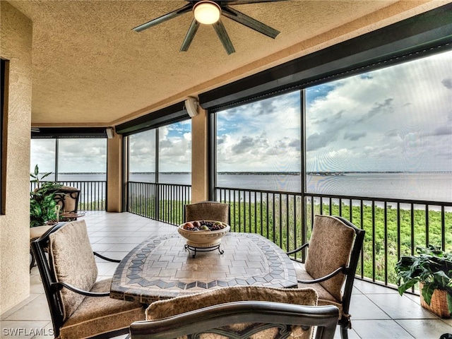 sunroom with ceiling fan and a water view