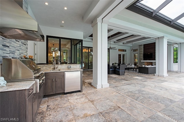 kitchen with light stone counters, a sink, wall chimney exhaust hood, stainless steel fridge, and dark brown cabinets