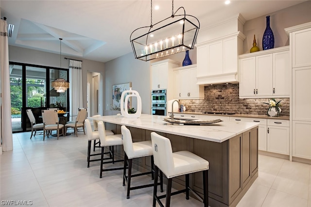 kitchen featuring white cabinetry, gas cooktop, decorative backsplash, double oven, and a notable chandelier