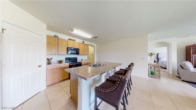 kitchen featuring sink, light tile floors, a breakfast bar, a center island with sink, and black appliances