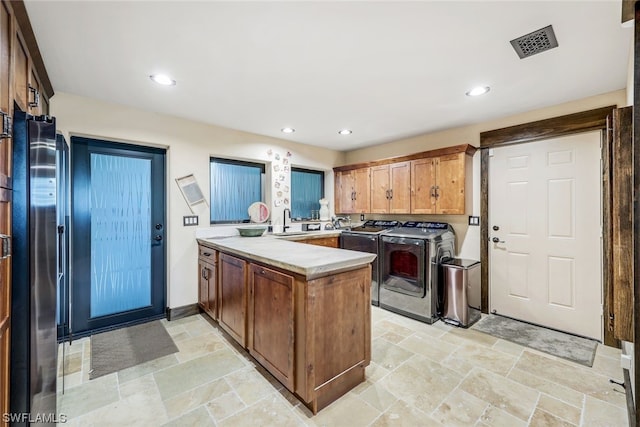 kitchen featuring kitchen peninsula, sink, washer and clothes dryer, and stainless steel refrigerator