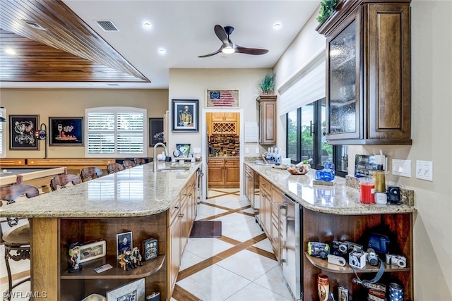 kitchen with light stone counters, wood ceiling, sink, a center island with sink, and a kitchen breakfast bar