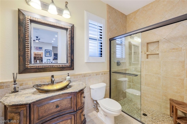 bathroom with ceiling fan, vanity, tile walls, a shower with shower door, and toilet