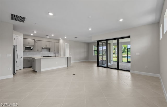 kitchen featuring stainless steel appliances, gray cabinetry, a center island with sink, tasteful backsplash, and light tile floors