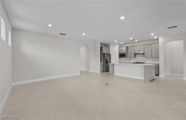 kitchen with stainless steel appliances, a kitchen island with sink, sink, and light tile floors