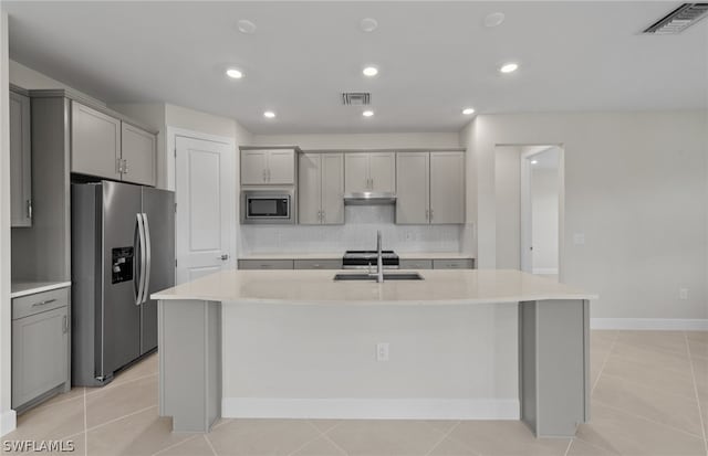 kitchen with light tile floors, a kitchen island with sink, and appliances with stainless steel finishes