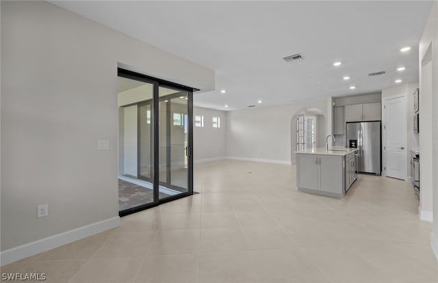 kitchen featuring stainless steel fridge, a center island with sink, light tile flooring, gray cabinetry, and a healthy amount of sunlight