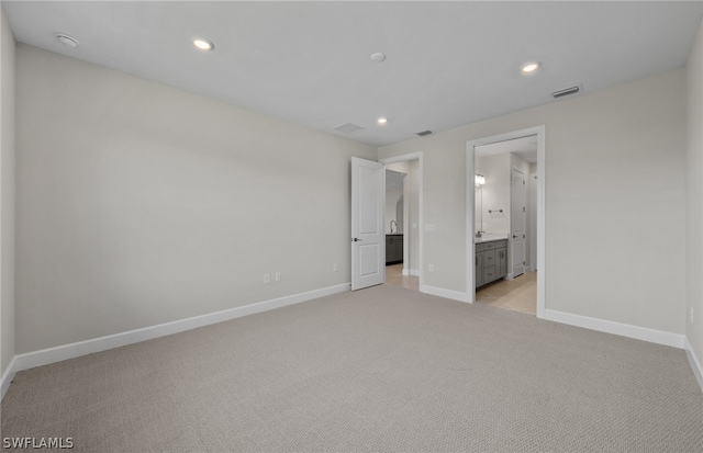 unfurnished bedroom featuring light carpet and ensuite bathroom