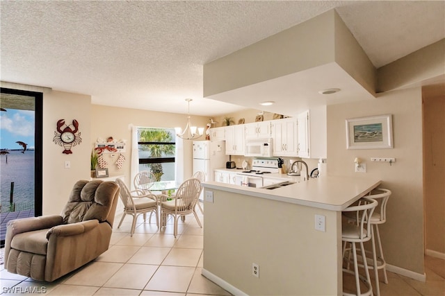 kitchen with kitchen peninsula, white appliances, light tile floors, hanging light fixtures, and a notable chandelier