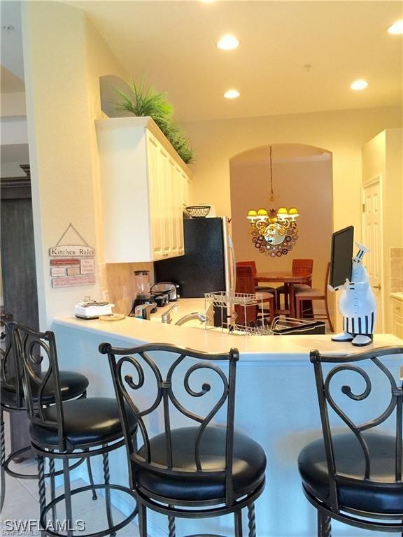 kitchen featuring an inviting chandelier, kitchen peninsula, a kitchen breakfast bar, white cabinetry, and black fridge