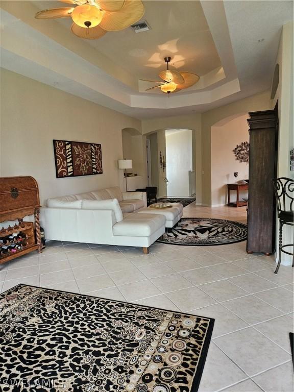 tiled living room featuring a raised ceiling and ceiling fan