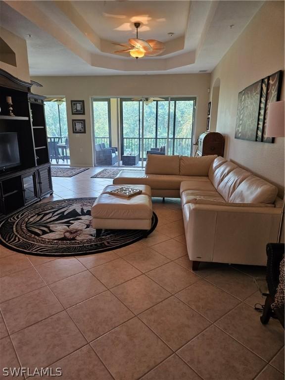 tiled living room featuring plenty of natural light, ceiling fan, and a raised ceiling