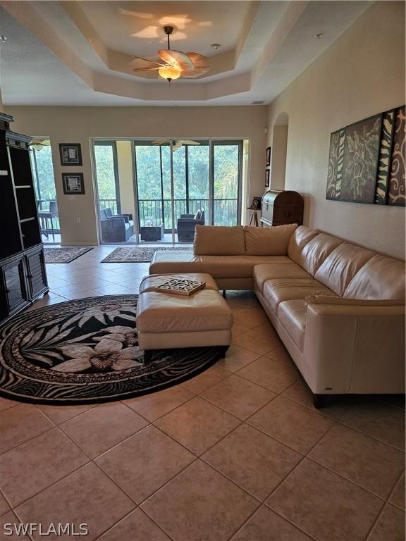 living room featuring tile patterned flooring, a raised ceiling, and ceiling fan