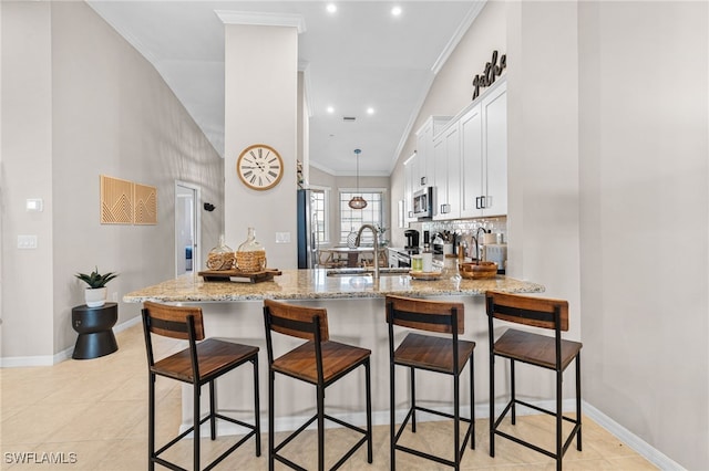 kitchen with light stone countertops, white cabinets, kitchen peninsula, and ornamental molding